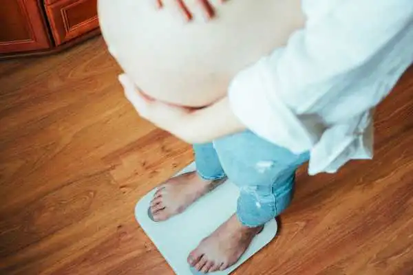 Image of woman weighing herself and experiencing weight gain through pregnancy Soham